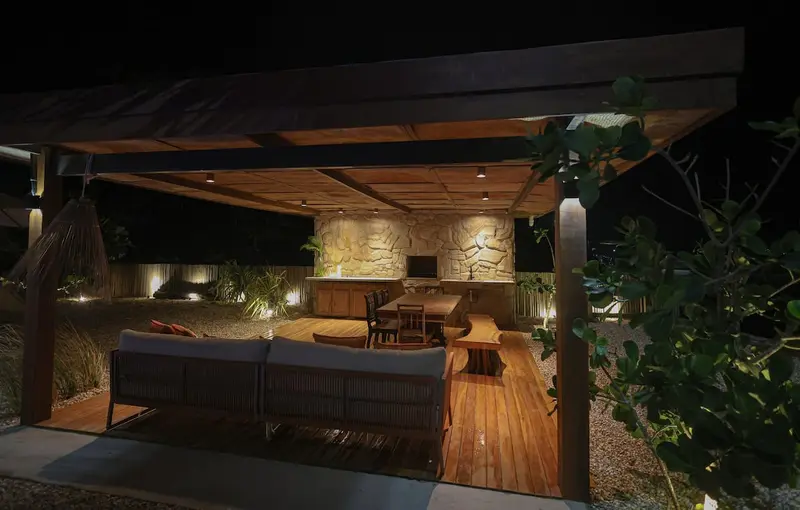Gazebo aceso à noite, com sofá, mesa e parede de pedra