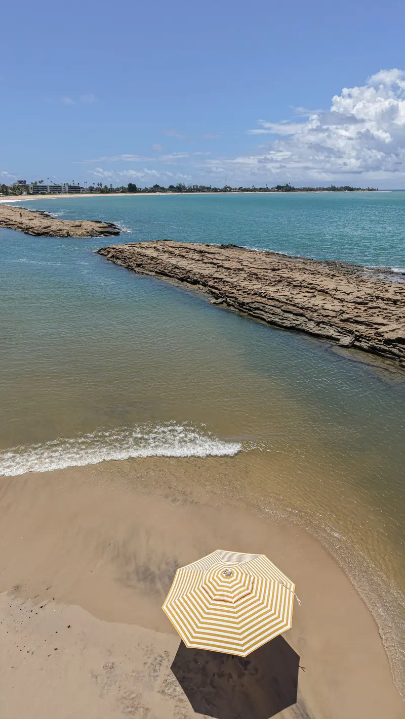 Praia vista de cima, com um guarda-sol listrado na areia