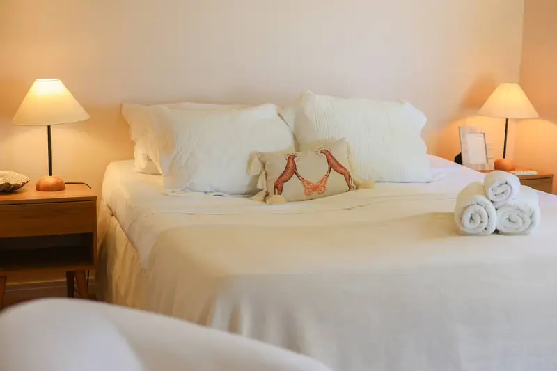 Cama com roupa de cama branca e toalhas enroladas, abajures acesos