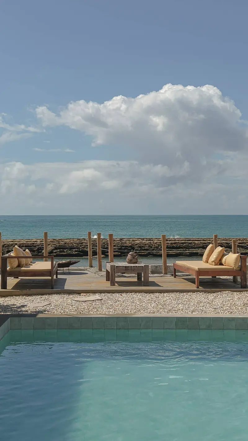 Deck de madeira com sofás voltado para o mar, atrás da piscina