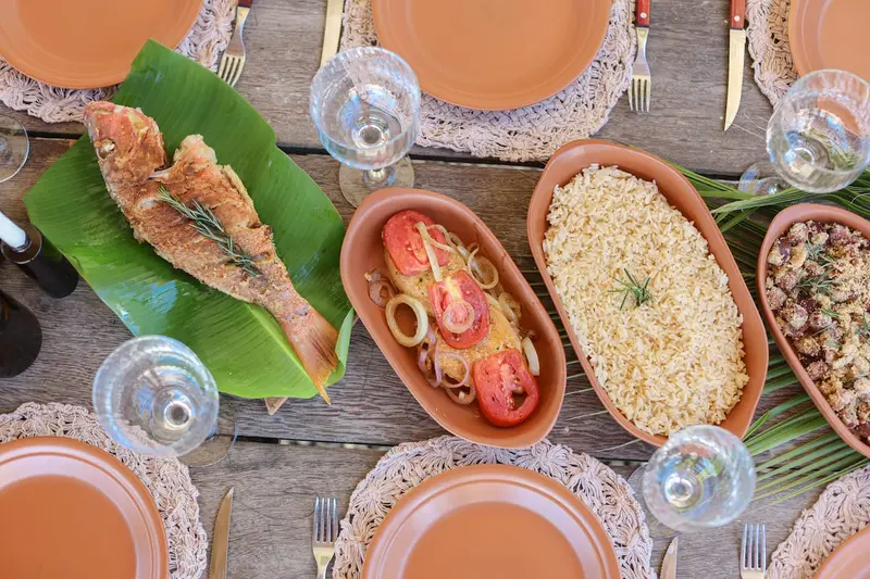 Pratos de barro com peixe, arroz e farofa, vistos de cima