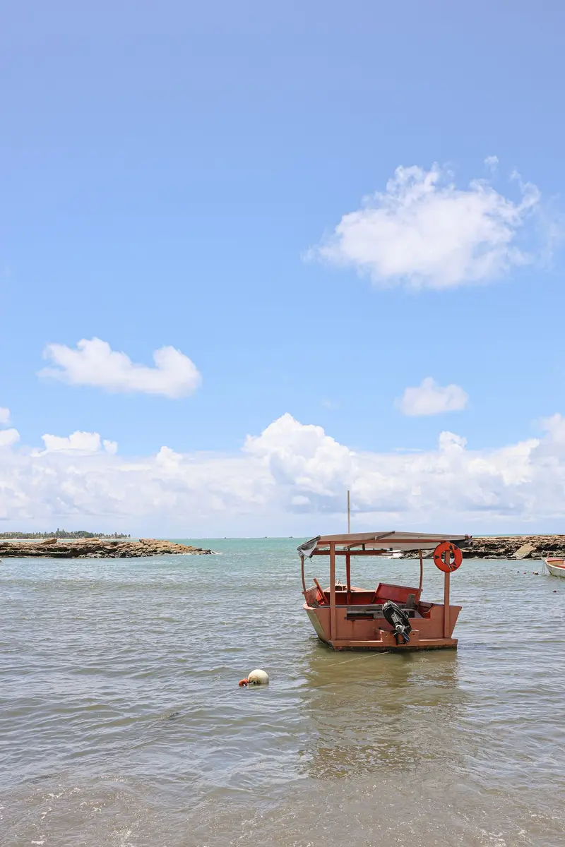 Barco vermelho de pesca em água rasa, com os arrecifes ao fundo