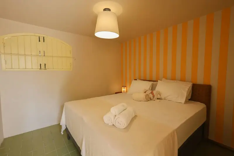 Quarto 4 no térreo, com cama de casal e parede listrada em ocre