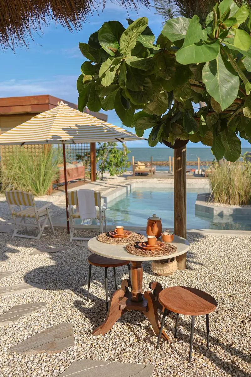 Mesa de café posta à beira da piscina, com guarda-sol e mar ao fundo