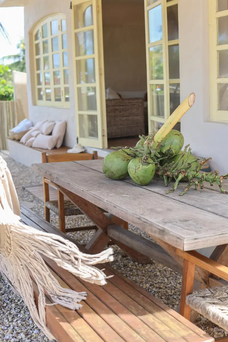 Mesa comprida de madeira no deck, com cocos verdes e redes ao lado