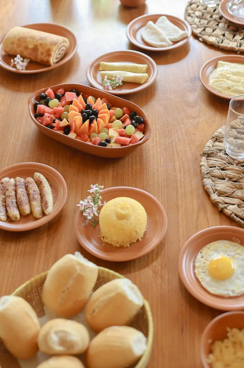 Mesa de madeira com pães, ovos, frutas e cuscuz em louça de barro