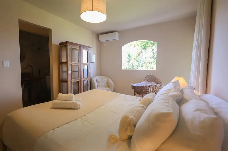 Quarto 2 com cama de casal, travesseiros e armário de madeira ao fundo