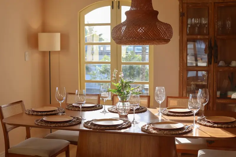 Sala de jantar com mesa de madeira posta e pendente de palha